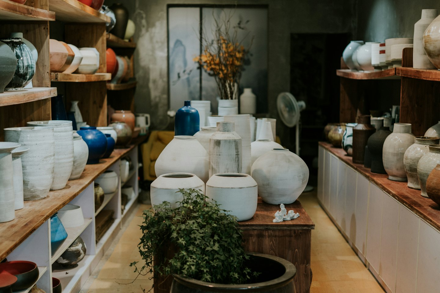Poterie en céramique faite à la main exposée sur des étagères et une table en bois.