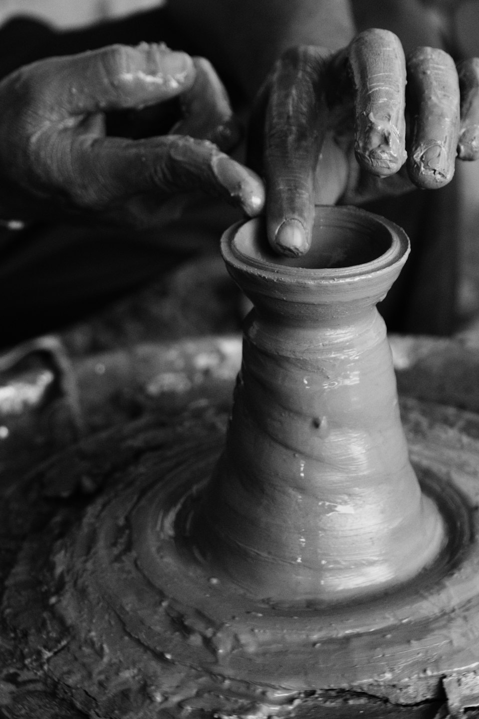 Mains couvertes d'argile façonnant un pot sur un tour de potier.