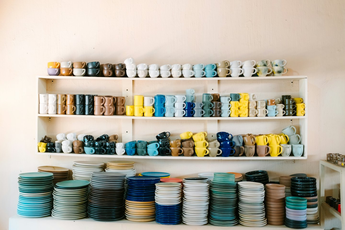 Assiettes et tasses en céramique artisanales disposées sur des étagères en bois.