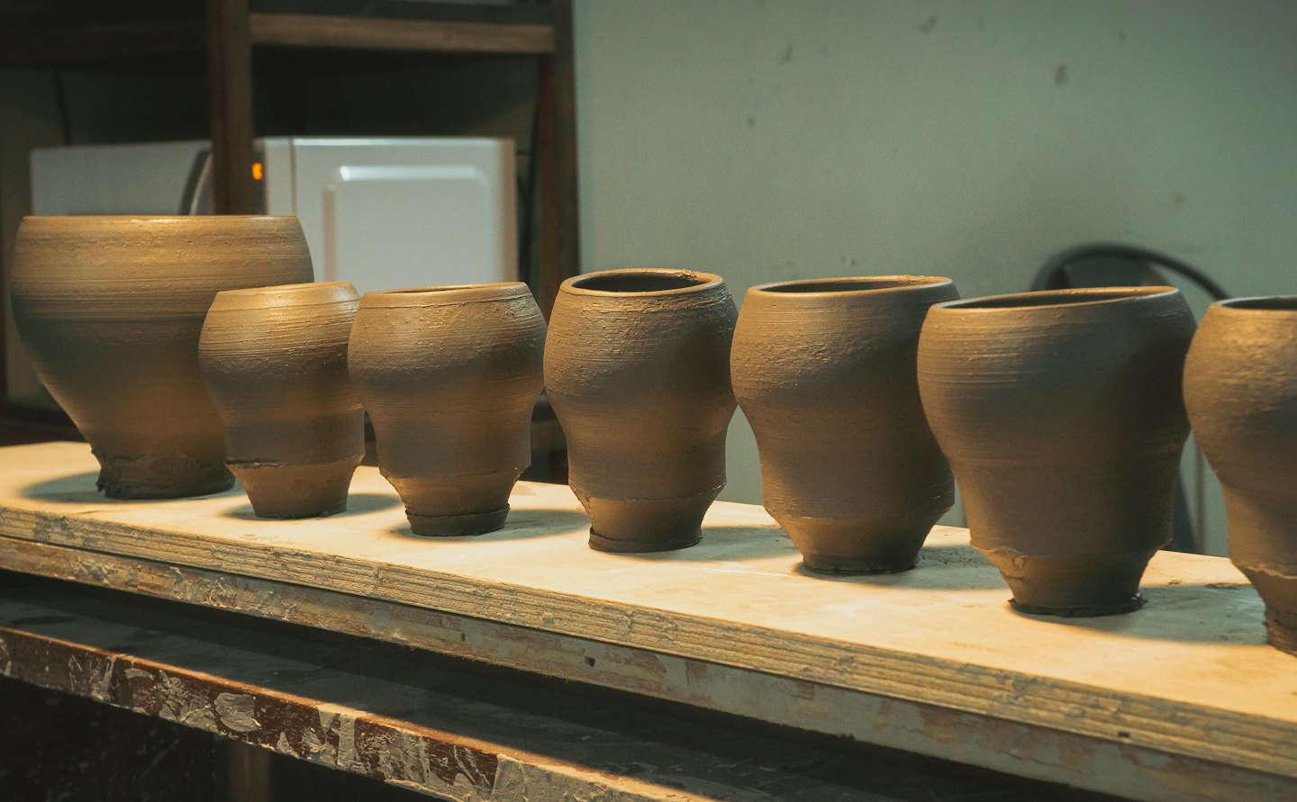 Pièces de poterie en argile non cuite séchant sur une étagère en bois.